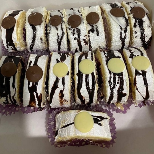 Sliced log cake served in individual stretched patty pan paper purple polka dot cup cake holders, log cake has white cream covering the outside , drizzled chocolate, and white and brown chocolate buttons